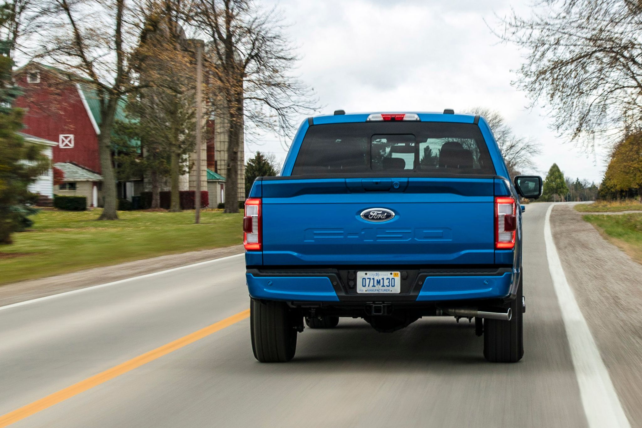blue truck on road with red barn to the left